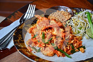 Thai food, stir fry rice noodles with shrimps, tofu, vegetable and crushed peanuts or pad thai on wooden table background