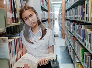 Thai girl student in uniform reading a book in library