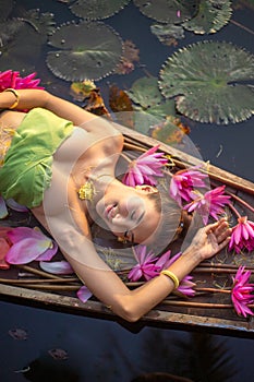 Thai girl in traditional Thai northern traditional costume in red lotus pond with wooden boat, identity culture of Thailand.