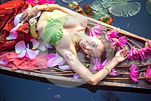 Thai girl in traditional Thai northern traditional costume in red lotus pond with wooden boat, identity culture of Thailand.