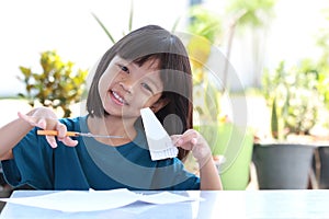 Thai girls aged 4 to 6 years sitting outside. Looks cute and bright. In the hand were scissors and paper. She is learning to cut