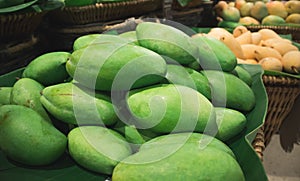 Thai green mango in basket with yellow mango background