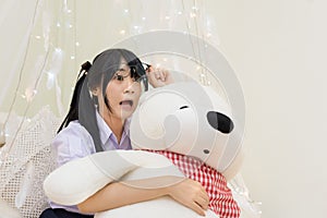 Thai high school girl in glasses show shocking expression while hugging teddy bear