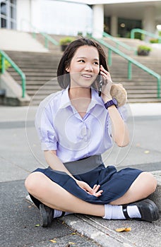 Thai high schoolgirl student in school uniform sit and chat on mobile