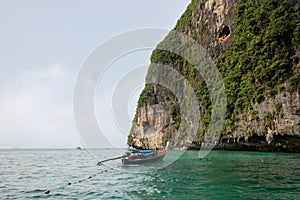Thai long tail boat and unidentified tourists snorkel near the entrance at the Viking Cave of Phi Phi Ley Island, Thailand