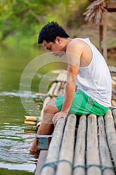 A Thai man in white tank top sitting on the bamboo raft