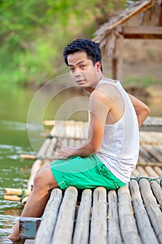 A Thai man in white tank top sitting on the bamboo raft