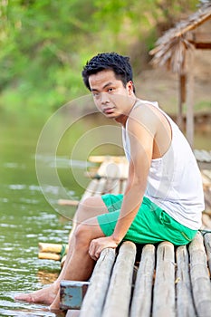 A Thai man in white tank top sitting on the bamboo raft