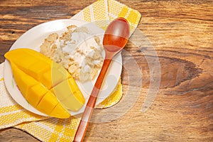 Thai mango and sticky rice with coconut milk desserts on white dish with wooden background. Mango is Thailand`s tropical fruit.