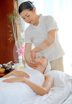 Thai masseuse do face massage for  young beautiful girl who lie and look up on bed in spa room with day light