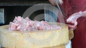 Thai merchant butcher is chopping a whole raw pork meat into pieces with a chopping knife, ready for sale in local outdoor superma