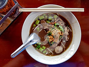 Thai noodle soup with meatball and pork stewed served in a white bowl.