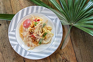 Thai papaya salad on a plate, papaya salad with poop, lemon, pepper, red tomato in white bowl on wooden table