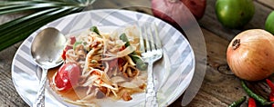 Thai papaya salad on a plate, papaya salad with poop, lemon, pepper, red tomato in white bowl on wooden table