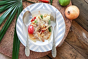 Thai papaya salad on a plate, papaya salad with poop, lemon, pepper, red tomato in white bowl on wooden table