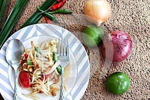 Thai papaya salad on a plate, papaya salad with poop, lemon, pepper, red tomato in white bowl on wooden table