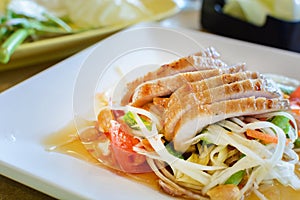 Thai papaya salad on white dish with grilled pork
