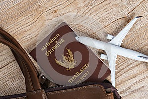 Thai passport, Leather bag and Small plane model on wooden board background