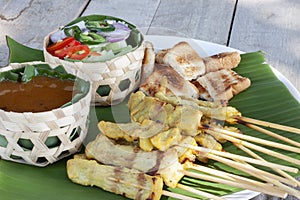 Thai pork satay, peanut sauce,  cucumber salad and grill bread in white plate.