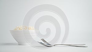 Thai steamed rice in a bowl with a spoon and black chopsticks placed on the side. On a white backdrop
