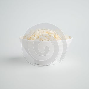Thai steamed rice in a bowl with a spoon and black chopsticks placed on the side. On a white backdrop