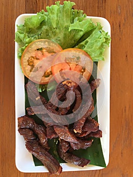 Thai style grilled pork with lettuce and tomato on wooden table.