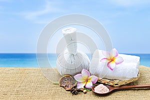 Thai style herbal massage ball with pink salt and dry herbs over blurred beach background