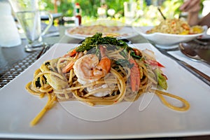Thai style spaghetti Pad Kee Maw with shrimp, corn, carrot, and fried basil in the white plate