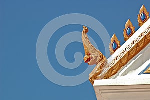 Thai traditional naga decoration on temple roof under blue sky