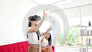 Thai woman lifestyle at home with Asian friend.Wearing virtual reality headset for playing online game.