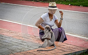 Thai woman in sarong and white fedora looking at Duskey monkey