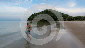 Thai woman in shorts and hat standing barefoot on beach at low tide