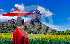 Thai woman in a Thai Lana dress holds an umbrella to watch a sunflower field photo