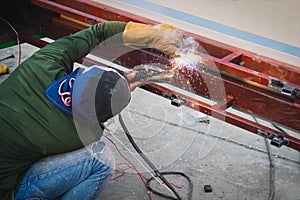 Thai worker man working clothes welds a metal pipe with arc welding machine in construction site with sparks bright lights and