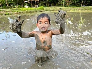 Thailand Asia boy is enjoy playing in the mud of rice field. Outdoor kid learning activity.