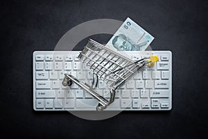 Thailand currency, White computer keyboard, Miniature shopping cart, Black background, Online shopping concept in stores, Low