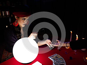 THAILAND - DEC 19, 2019: Asian astrologer woman holding customer hand and use palmistry skill with magnifying glass for zoom the