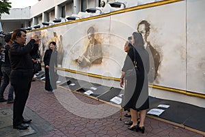 Thais in black mourning clothes are photographed at a wall with the image of the dead king Bhumibol Adulyadej. A fragment of funer