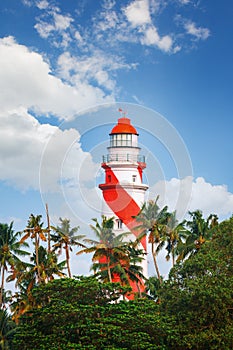 Thangassery Lighthouse on the cliff surrounded by palm trees and big sea waves on the Kollam beach. Kerala, India