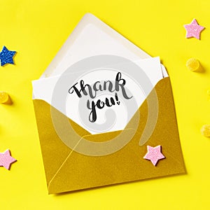 Thank you card in a golden envelope, overhead square shot on a yellow background