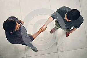 Thank you for coming in today. High angle shot of two young businessmen shaking hands in agreement inside of the office