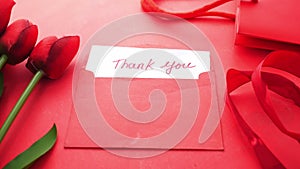 thank you message, gift and tulip flower envelope on red background