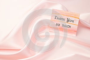 Thank-you note with Thank You so much inscription on pastel pink silk background: the concept of manifestation of gratitude and