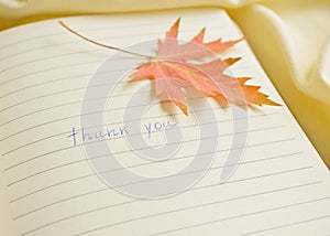 Thank you text message on paper page background with printed lines and decorative of colorful maple leaf