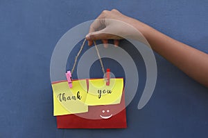 Thank you vintage style word on colorful origami paper notes. Young girl holding thank you sign rope with smiling emoticon on blue