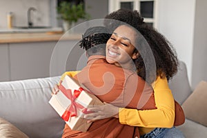 Thankful African Lady Hugging Her Husband Receiving Romantic Gift Indoors