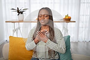 Thankful black woman sitting on sofa in living room, gesturing