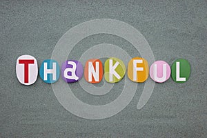 Thankful, creative word composed with multi colored stone letters over green sand