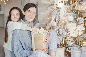 Thankful small female child embraces her mother who gave present, spend wonderful unforgettable time together, celebrate Christmas