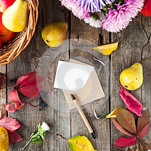 Thanksgiving background with seasonal fruits, flowers, greeting card and envelope on a rustic wooden table. Autumn harvest concept